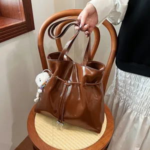 Detailaufnahme einer braunen Lackleder-Umhängetasche mit Kordelzug und Anhänger.