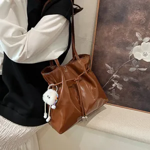 Detailansicht der stilvollen braunen Lackleder Umhängetasche mit süßem flauschigen Anhänger.