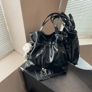 Detailansicht einer glänzenden schwarzen Schultertasche mit niedlichem Plüschanhänger.