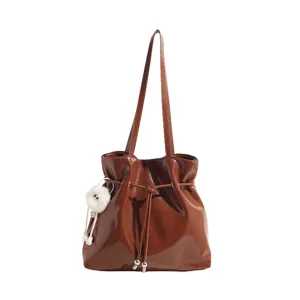 Braune Schultertasche aus Lackleder für Damen, stylische Beuteltasche mit flauschigem Anhänger.