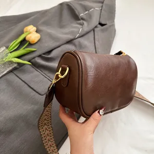 Detailaufnahme der braunen Zylindertasche mit strukturiertem breitem Riemen und Goldbeschlag.