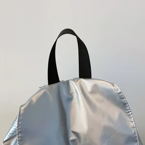 Detailaufnahme der metallisch silbernen Rucksackoberseite mit schwarzem Stoffgriff und Textur.