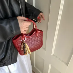 Detailaufnahme der roten Leder-Flecht-Handtasche mit Perlenanhänger, eleganter Vintage-Look.