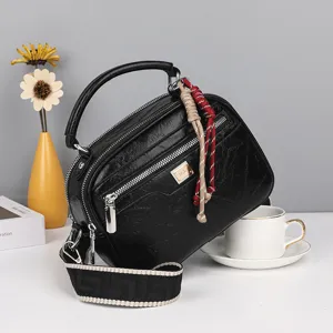 Schwarze Boston Handtasche aus Ölwachsleder mit breitem gemustertem Gurt und Metalldetail.