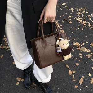 Schicke braune Handtasche aus Kunstleder mit süßem Plüschbären, ideal für den Herbst.
