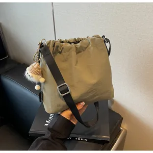 Lässige Nylon Eimer Tasche für Damen, Umhängetasche mit süßem Puppenanhänger und breitem Gurt.