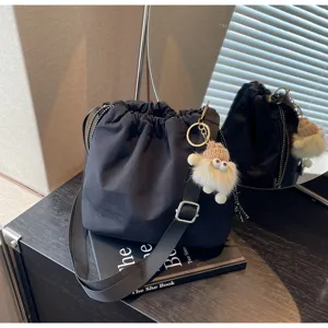 Detailaufnahme einer schwarzen Nylon-Beuteltasche mit Kordelzug und süßem Plüschpuppen-Anhänger.