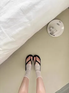 Close-up detail of ultra-thin sheer Korean style socks paired with casual black sandals on soft carpet.
