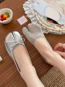 Close-up detail of tabi split-toe socks and silver ballet flats on wooden tabletop background.