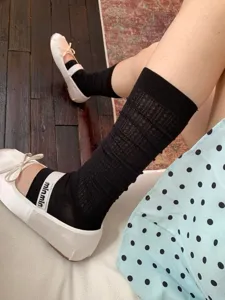 Close-up detail shot of women's black mesh calf socks with ballet style white flat shoes.