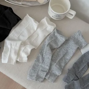 Detailed shot of stylish ballet style stirrup leg warmers in white, grey, and black colors.