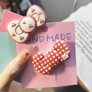 Close-up view of the cute red plaid and cherry bow hair clips on pink display card.