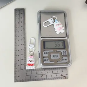 Vista dettagliata portachiavi cane bianco carino con dimensioni e peso su bilancia borsa.