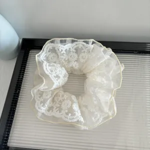 Gros plan sur le chouchou en dentelle blanche, avec des volants en tulle et motif floral.