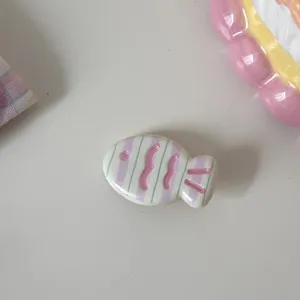 Close-up detail of a cute ceramic fish hair clip in pastel pink and green stripe design.