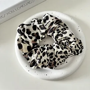 Close-up view of stylish leopard print satin hair scrunchie on decorative white tray.
