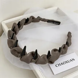 Detail shot of brown woven fabric headband featuring black teeth and handmade tag on mesh.