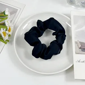 Close up photo of a black silk hair scrunchie placed on a white plate with floral decor.
