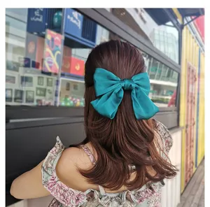 Detail shot of a large green satin bow hair clip, showing the smooth fabric and back view design.