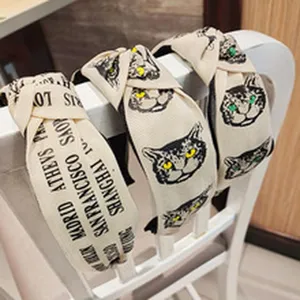 Detail view of wide fabric knotted headbands with cute cat face print and stylish city design.