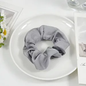 Detailed close-up of a soft gray hair scrunchie on a white plate with floral props.