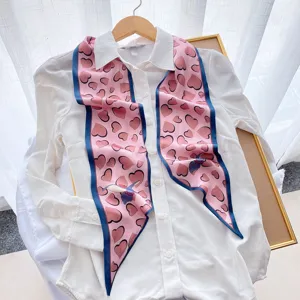 Detailed view of women's long silk scarf with pink heart print and elegant streamer design.