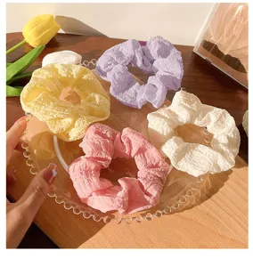 Close up detail of colorful puff crinkled hair scrunchies set on glass plate for daily styling.