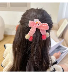 Lazo de pelo tejido en rosa con pompones bonitos para peinados infantiles diarios.