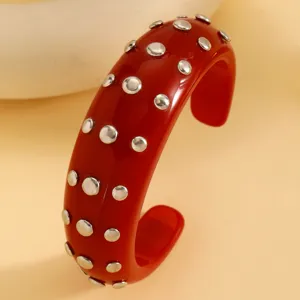 Red resin cuff bracelet with metal rivets, punk style fashion jewelry accessory for women.