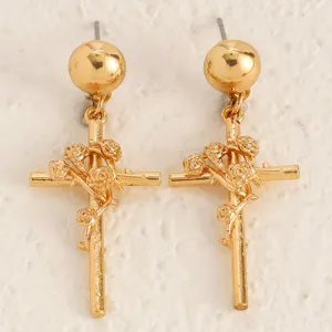 Gros plan de boucles d'oreilles croix et roses dorées aux détails métalliques floraux.