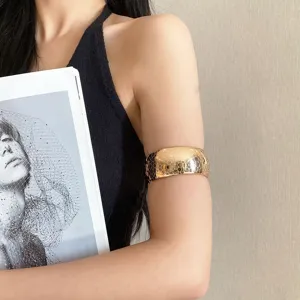 Detail view of a wide gold metal arm cuff bracelet, stylish fashion upper arm accessory detail.