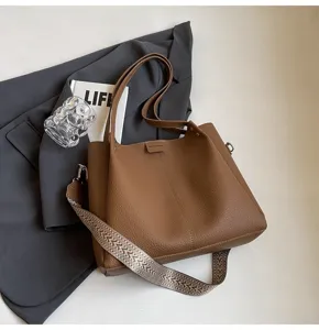 Brown leather bucket bag detail showing textured surface and wide patterned strap.