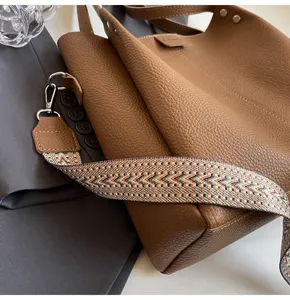 Detailed shot of a stylish brown leather bucket bag featuring a patterned wide strap and smooth texture.