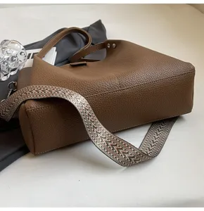 Detailed view of the brown leather bucket bag featuring a wide patterned woven strap.