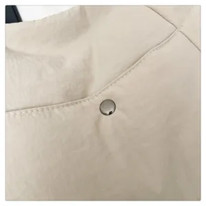 Detail view of the beige fabric tote bag showing fine stitching and a sleek metal snap button.