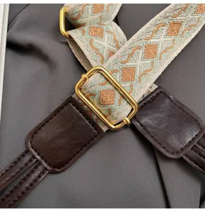 Detailed view of wide woven bag strap with geometric pattern, adjustable gold hardware, and leather.