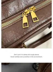 Close-up detail of brown leather handbag with golden double zippers and fine texture.