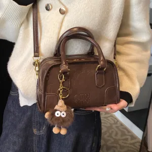 Brown boston shoulder bag for women, retro PU leather top handle crossbody bag with cute doll charm.