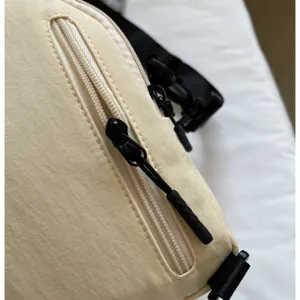 Vue détaillée de sac à bandoulière beige minimaliste, tissu résistant et fermeture éclair noire.