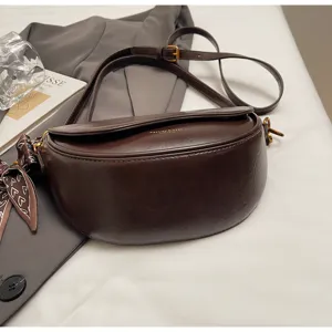 Dark brown saddle crossbody bag detail view, sleek leather texture with stylish side ribbon.