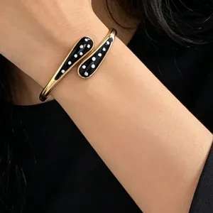 Close-up of gold-tone open bangle with black enamel white polka dot details on wrist.