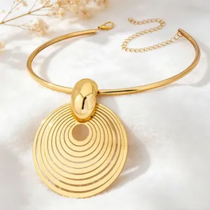 Close-up detail of a bold gold metal choker necklace featuring a large concentric ring pendant.