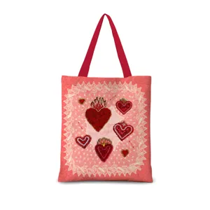 Gros plan sur le détail du sac fourre-tout rose avec des poignées rouges et un cœur brodé.