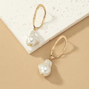 Vue de détail de boucles d'oreilles dorées géométriques avec perles baroques élégantes.