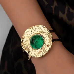 Hammered gold cuff bracelet with a large round green stone centerpiece, detailed view of elegant jewelry.