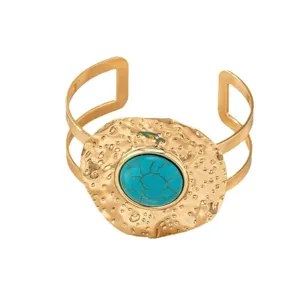 Elegant gold-tone hammered cuff bracelet featuring a striking central turquoise stone detail.