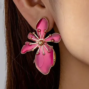 Close-up of bright pink floral earring with gold metallic details worn on earlobe.