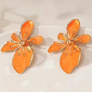 Detailed shot of bright orange flower earrings with golden outlines, perfect for summer.