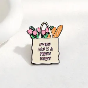 Close-up detail of the cute enamel pin featuring a shopping bag with tulips and baguettes.