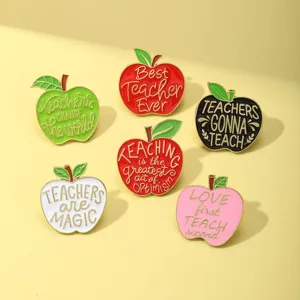 Close-up detail of cute apple enamel pins with inspirational teacher quotes, metal alloy.